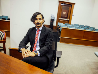 Person in suit with red tie sitting in a chair in a court room